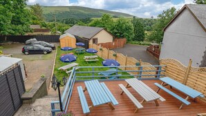 A deck with picnic tables and umbrellas, a wooden fence, and a car parked in the background. - The Elan Hotel (Rhayader)