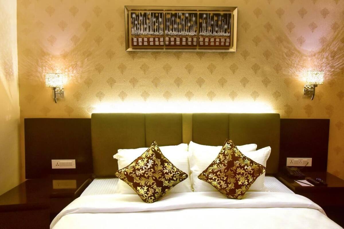 A hotel room with a bed, two nightstands, a wall-mounted shelf, and two wall sconces.