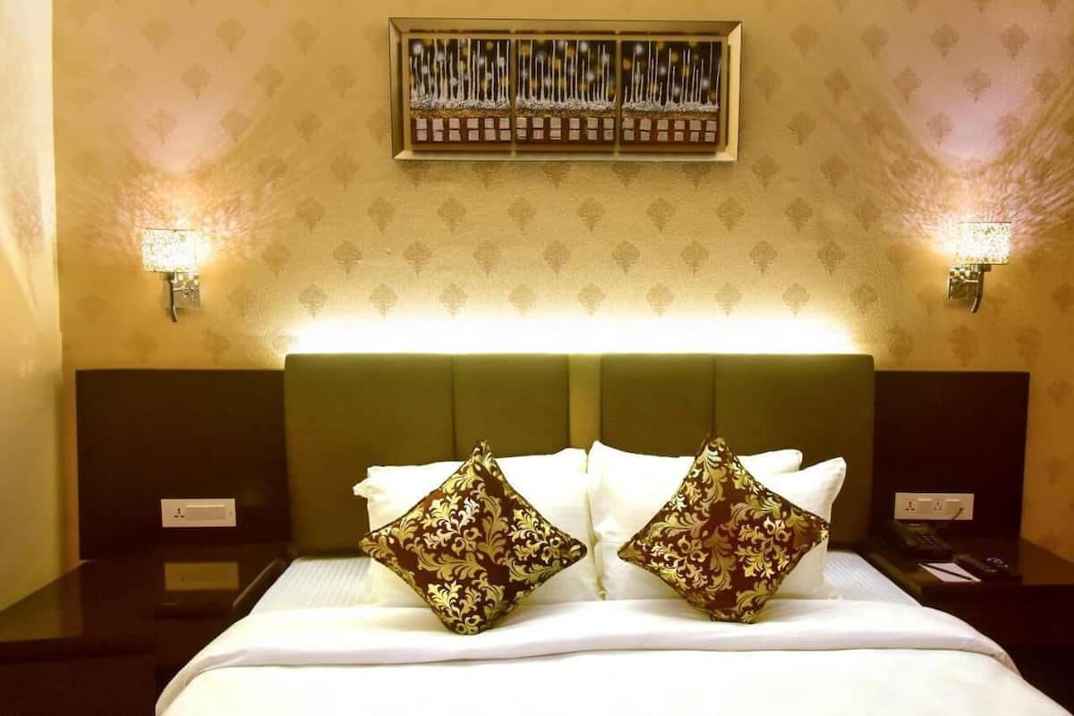 A hotel room with a bed, two nightstands, a wall-mounted shelf, and two wall sconces.