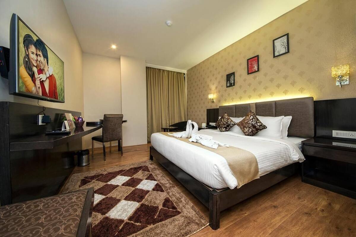 A hotel room with a bed, a desk, a chair, a TV, and a wall-mounted picture.