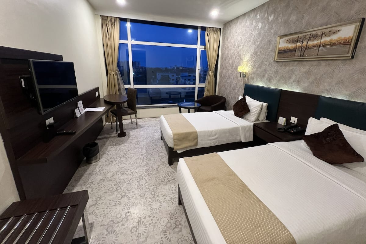 A hotel room with two beds, a desk, a TV, a chair, and a window with a city view.
