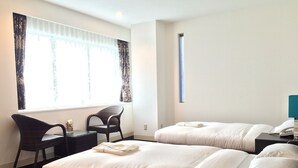 Hotellihuone, jossa on kaksi sänkyä, työpöytä, tuoli ja ikkuna, jossa on verhot.