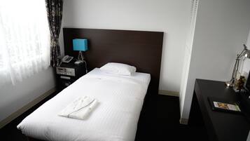 Habitación de hotel con una cama bien hecha, una mesita de noche con lámpara, un teléfono y un escritorio pequeño con una revista.