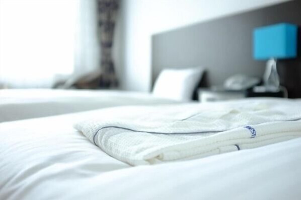 A neatly made bed with a white comforter and a folded white towel.