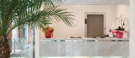 A reception desk with a marble counter, a palm tree, and two flower arrangements.