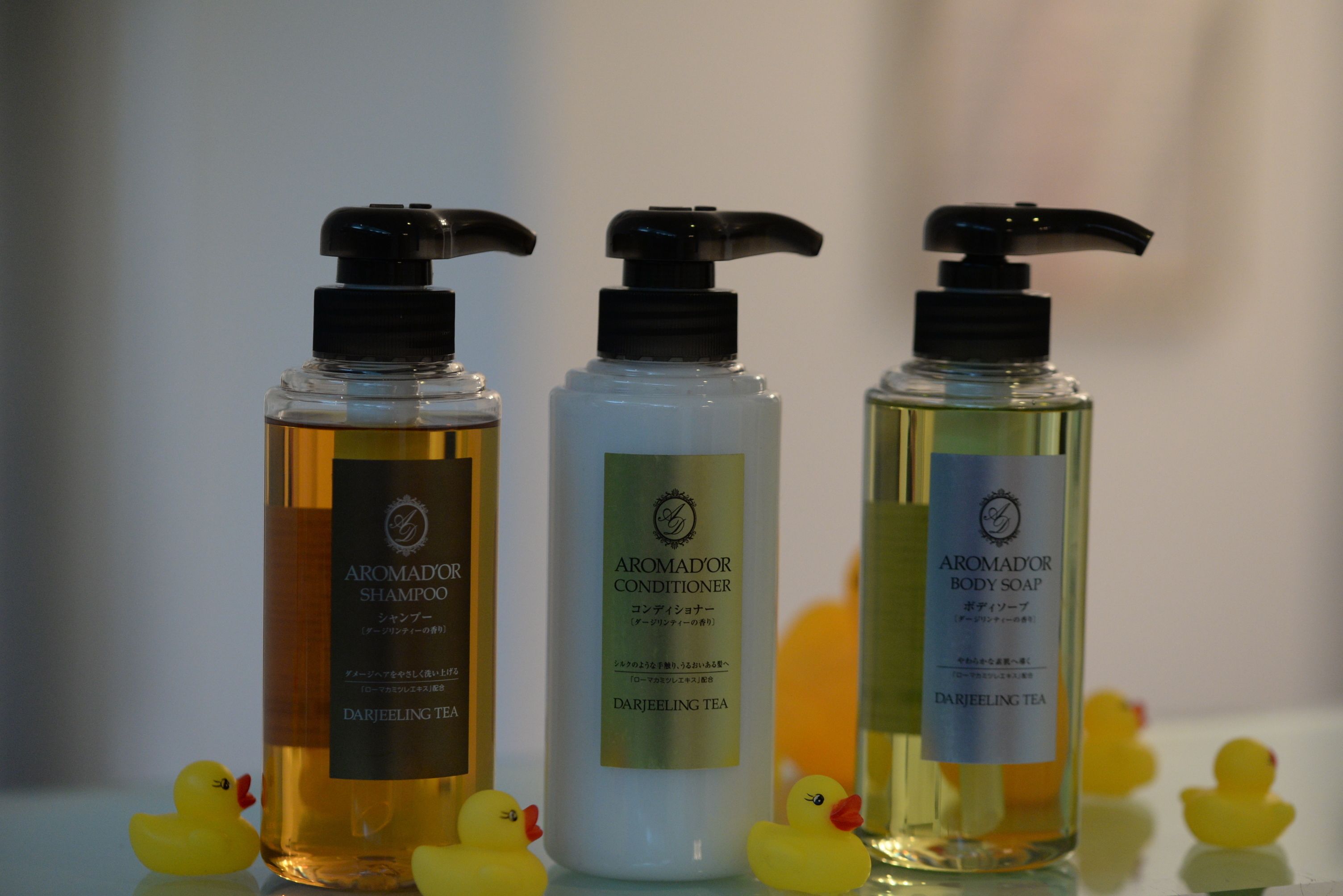 Three bottles of Aromadór products: shampoo, conditioner, and body soap, each with a pump dispenser.
