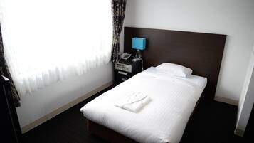 A hotel room with a neatly made bed, a bedside table with a lamp and phone, and a window with sheer curtains.