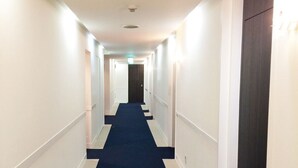 Hotellin käytävä, jossa on sininen matto, valkoiset seinät ja ovet molemmilla puolilla.