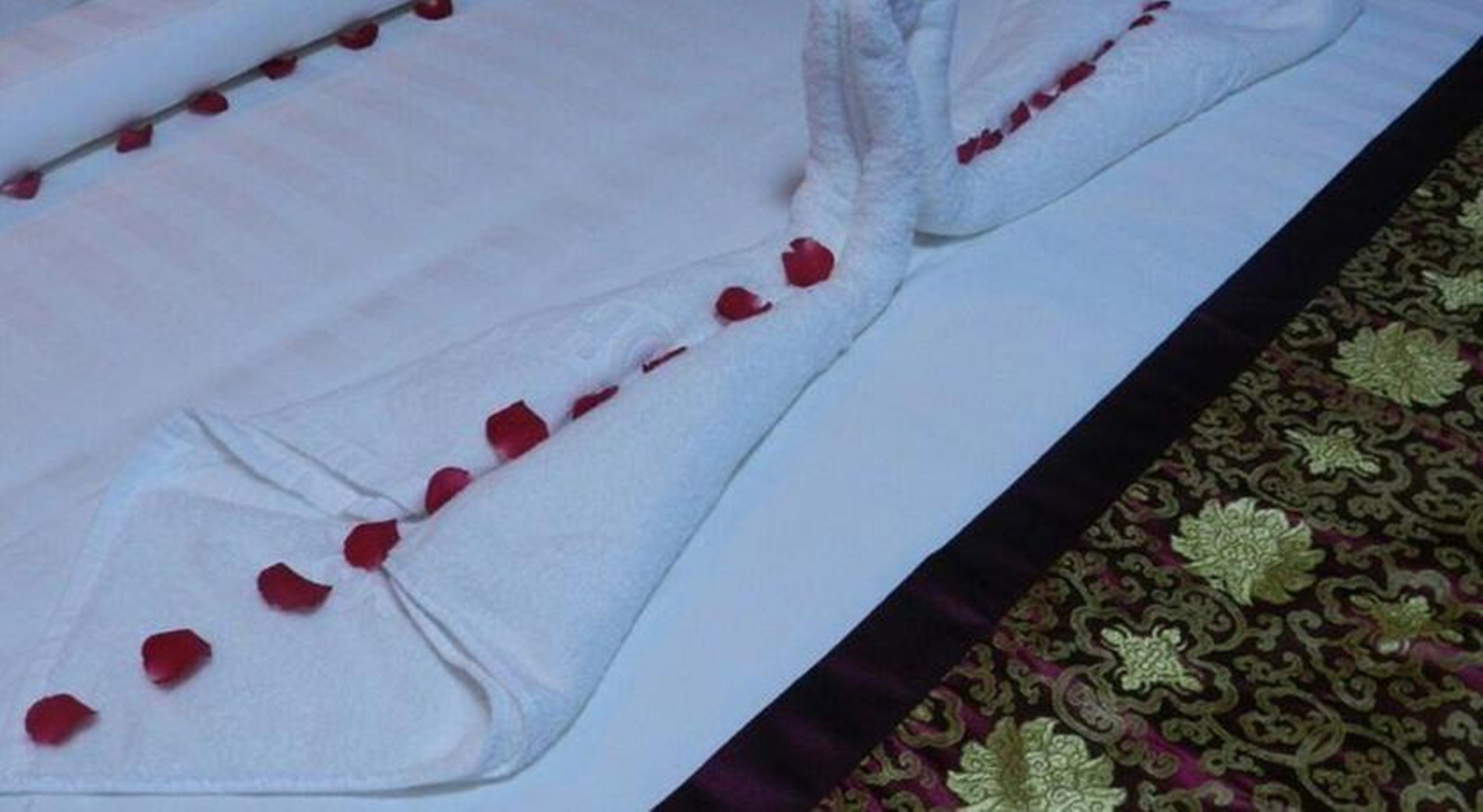 A bed with white sheets and red rose petals arranged along the edge.