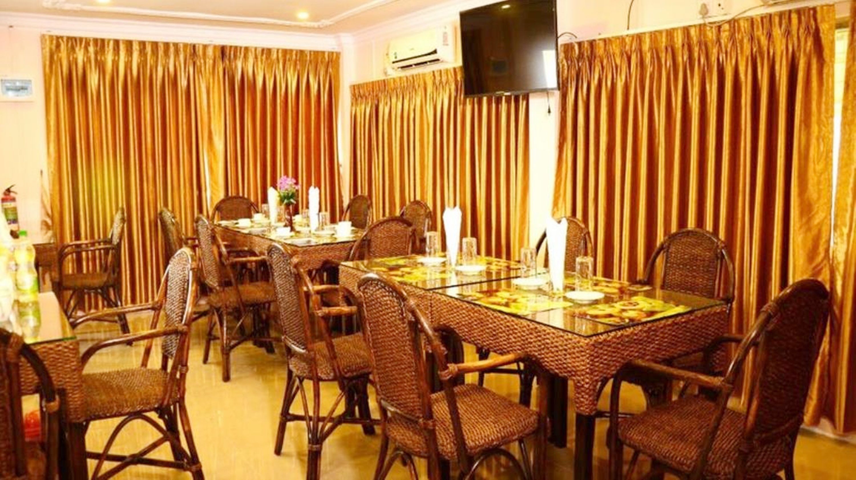 A dining area with a glass table, wicker chairs, and gold curtains.