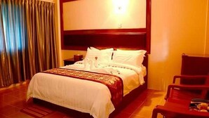 A hotel room with a large bed, a wooden headboard, a nightstand, a chair, and a curtain. - Real Link Hotel (Yangon)