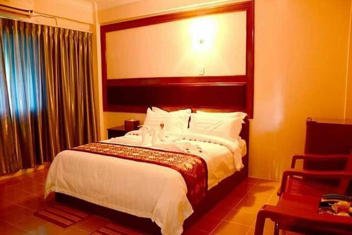 Habitación de hotel con una cama grande, cabecera de madera, mesita de noche, una silla y una cortina.
