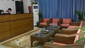 A reception area with a wooden desk, wicker chairs, a glass coffee table, and a blue curtain in the background. - Real Link Hotel (Yangon)