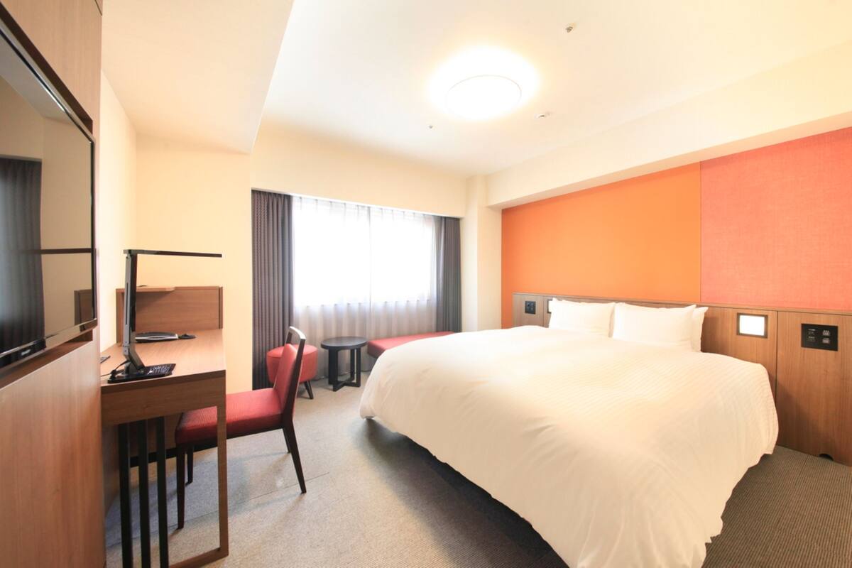Et hotelværelse med en stor seng, et skrivebord med en computer, en stol og et lille bord.