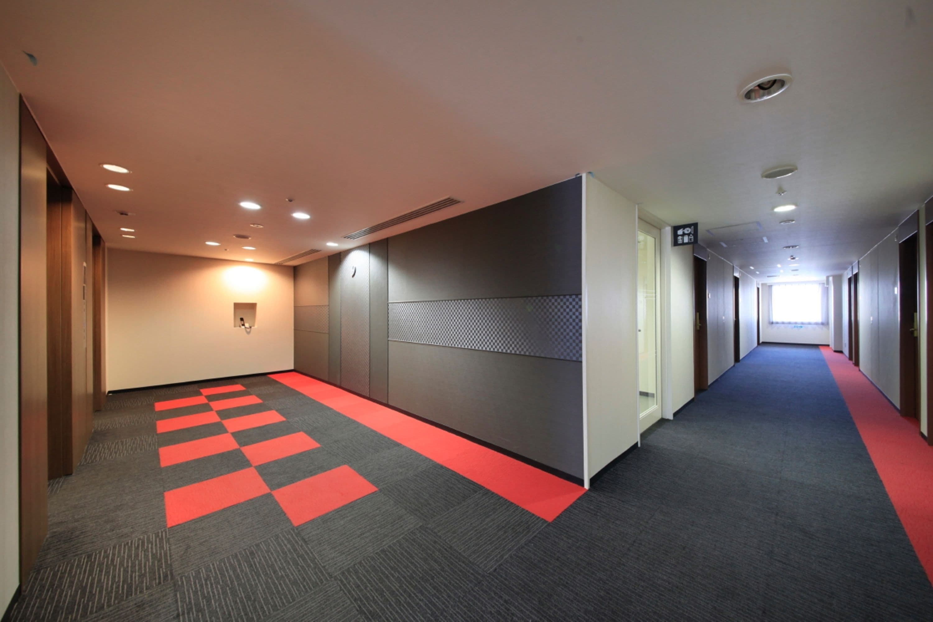 A hallway with a red and grey carpet, a wall-mounted light, and a door at the end.