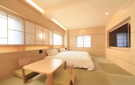 A modern hotel room with tatami flooring, a bed, a TV, and a small table.