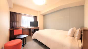 Una habitación de hotel con cama, escritorio con televisor, una mesita y una silla roja.