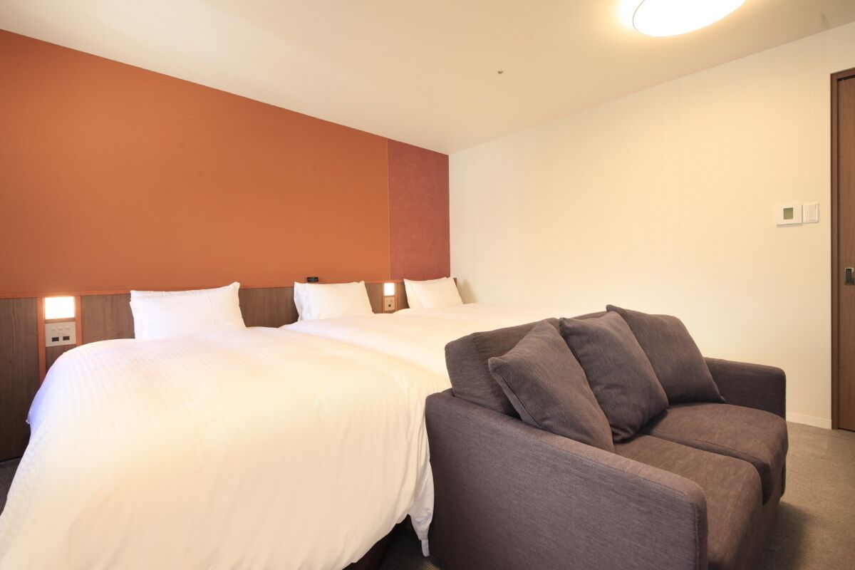 Habitación de hotel con dos camas, un sofá y un cabecero de madera.