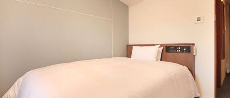 A hotel room with a large bed, a wooden headboard, and a light-colored wall.