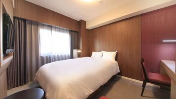A hotel room with a large bed, a desk, a chair, a small table, and a window with curtains.