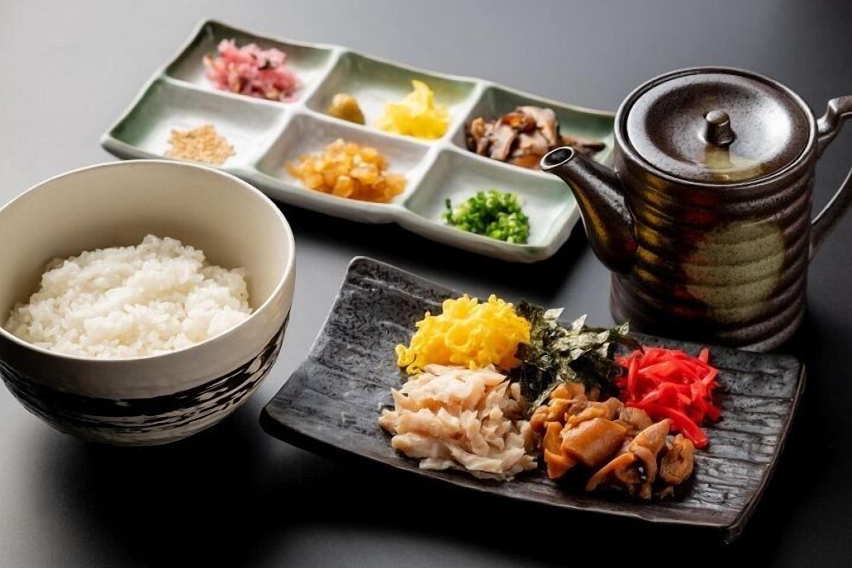 A traditional Japanese meal setup with a bowl of rice, a multi-compartment dish with various ingredients, and a teapot.