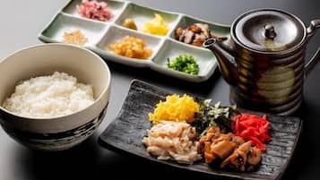 A traditional Japanese meal setup with a bowl of rice, a multi-compartment dish with various ingredients, and a teapot.