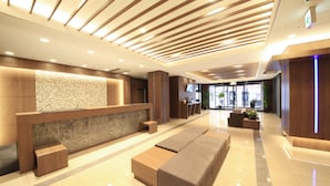 A modern hotel lobby with a reception desk, seating area, and a large window providing a view of the city.