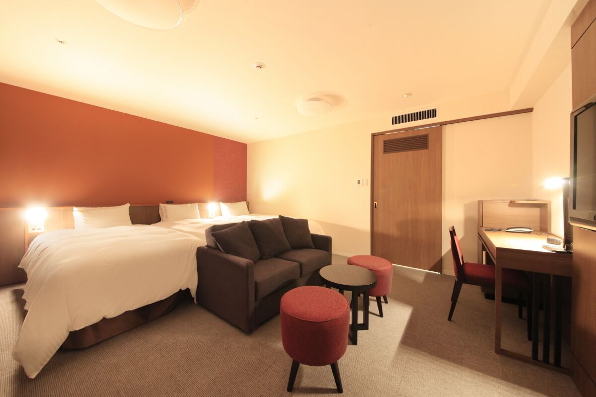A hotel room with a bed, a sofa, a desk, a chair, and a small table.