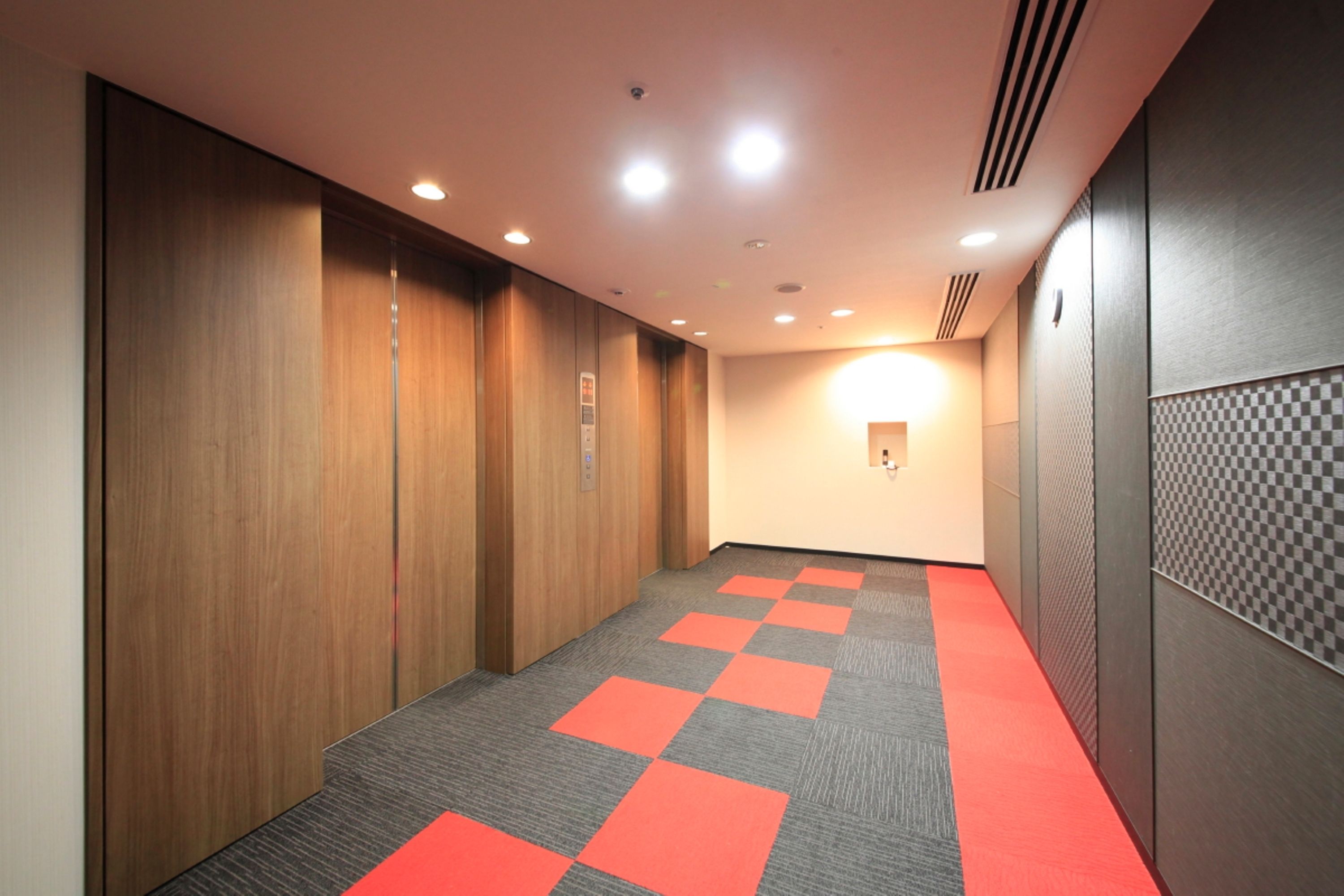 A hallway with wooden lockers, a red carpet, and a checkered wall panel.