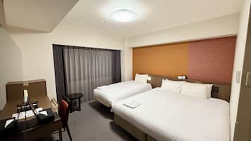 Habitación de hotel con dos camas, un escritorio, una silla, una mesita y un ventanal con cortinas.