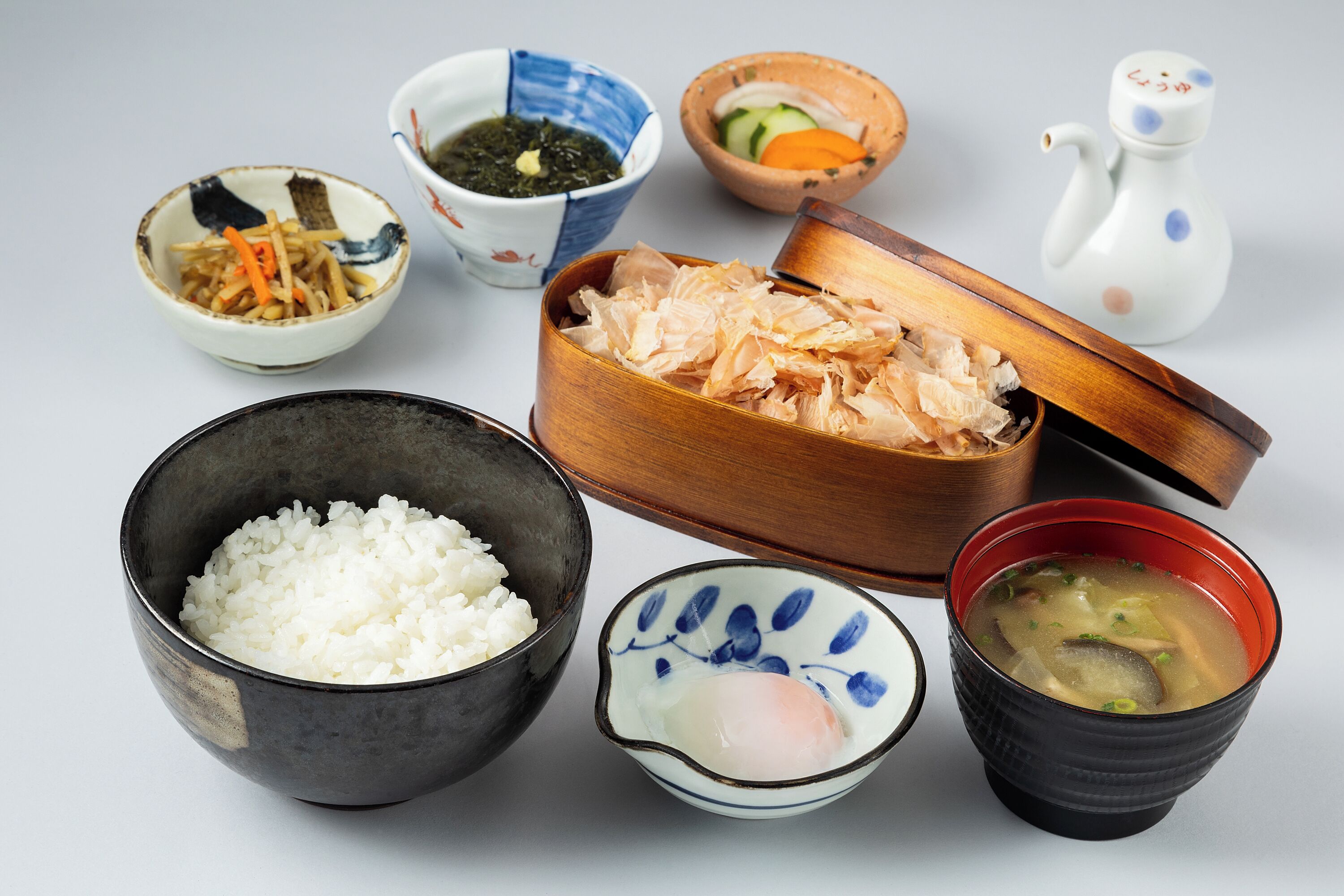 A variety of Japanese dishes including rice, miso soup, and a bowl of shredded fish.