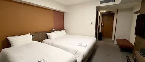 A hotel room with two beds, a flat-screen TV, a bench, and a door leading to another room.