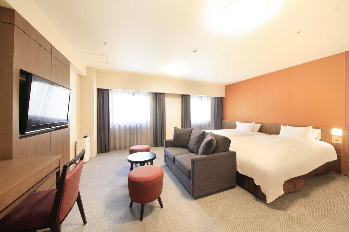 Et hotelværelse med seng, sofa, fjernsyn og to pudestole.