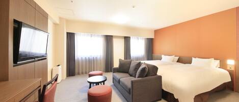 A hotel room with a bed, sofa, TV, and two ottomans.