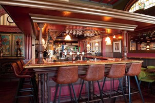 A bar area with a long counter, bar stools, and a variety of bottles and glasses.