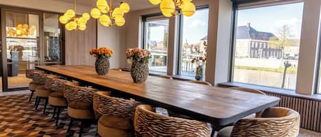 A modern dining area with a long table, zebra-patterned chairs, and large windows with a view.