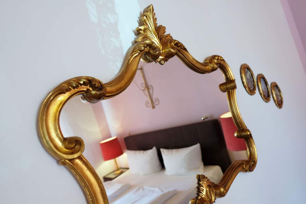 Ein Zimmer mit einem Bett, einem Nachttisch und einem Spiegel mit aufwändiger Goldverzierung.