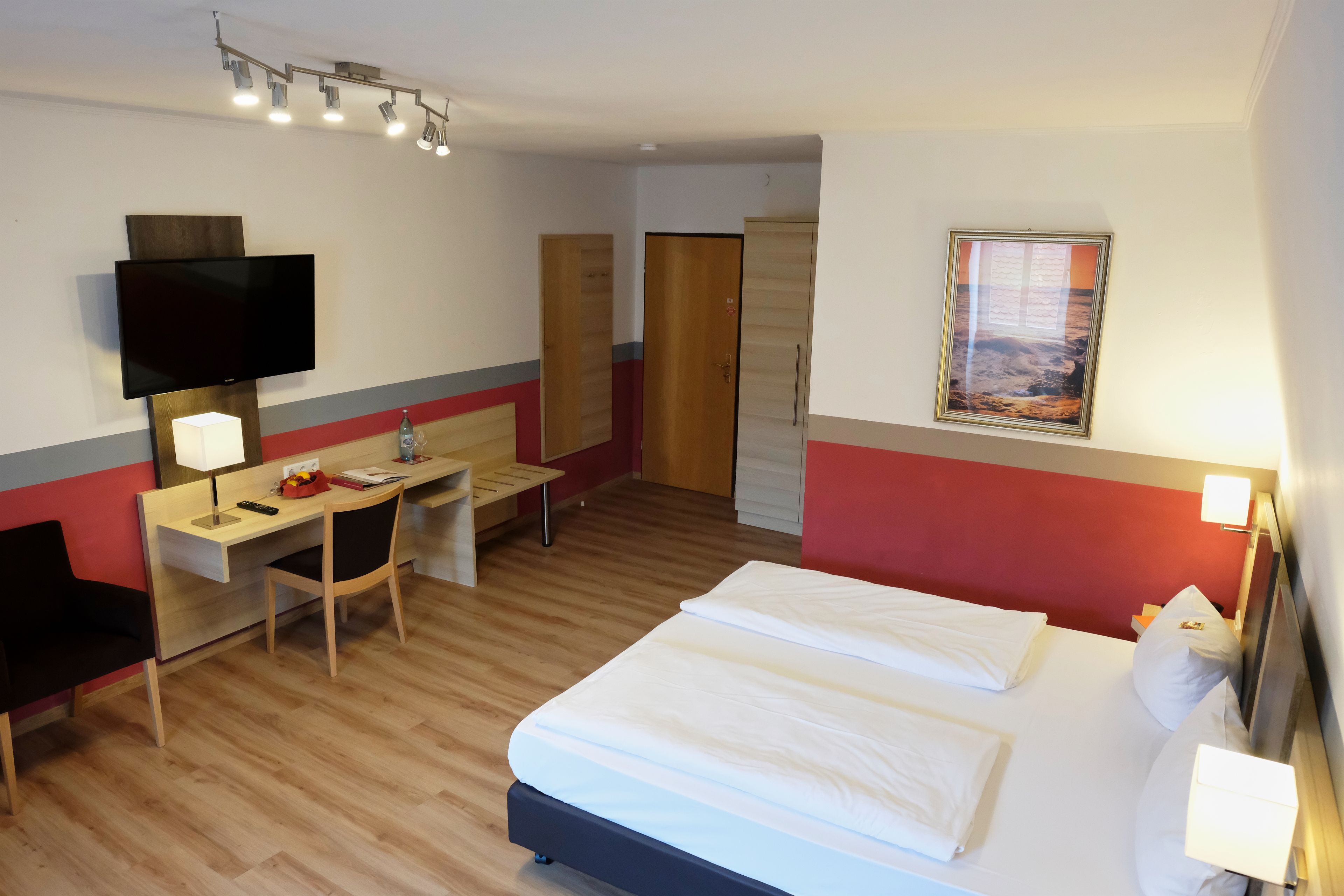 A hotel room with a bed, desk, chair, TV, and a framed picture on the wall.