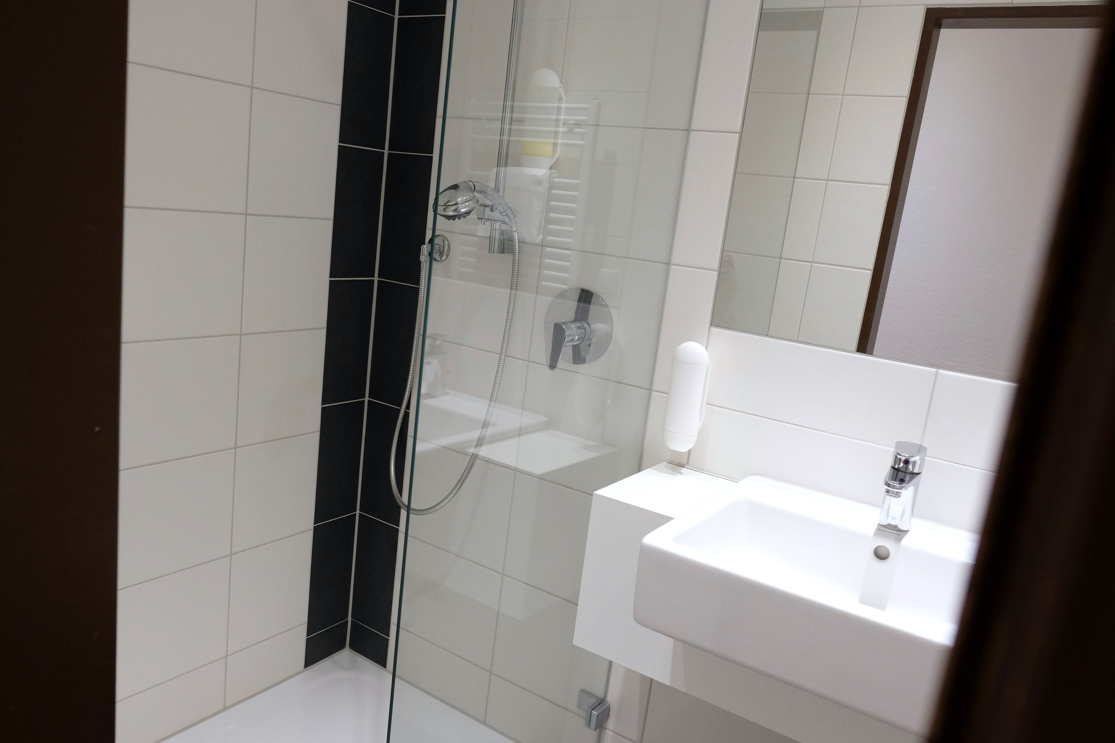 A modern bathroom with a glass-enclosed shower, a white sink, and a mirror.