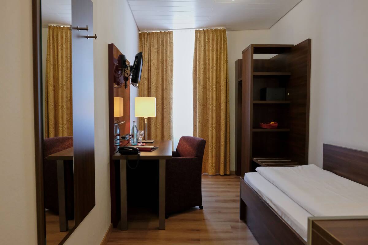 Ein Hotelzimmer mit einem Bett, einem Schreibtisch mit Stuhl, einer Lampe, einem Fernseher und einem Kleiderschrank.