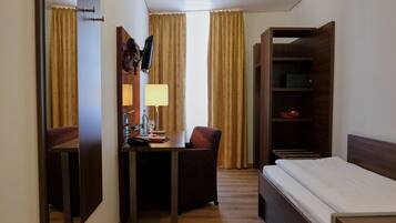 A hotel room with a bed, a desk with a chair, a lamp, a TV, and a wardrobe.