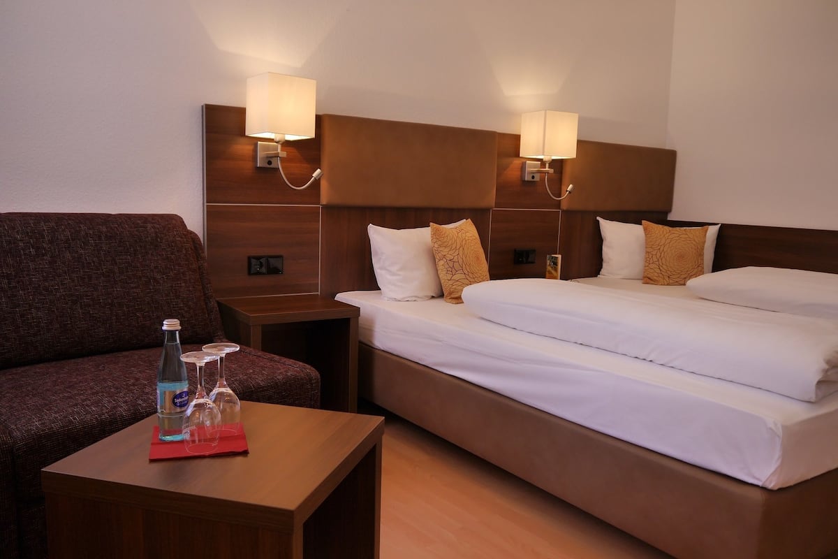 Ein Hotelzimmer mit Bett, einer Couch, einem Nachttisch und einem Tisch mit Flasche und Gläsern.