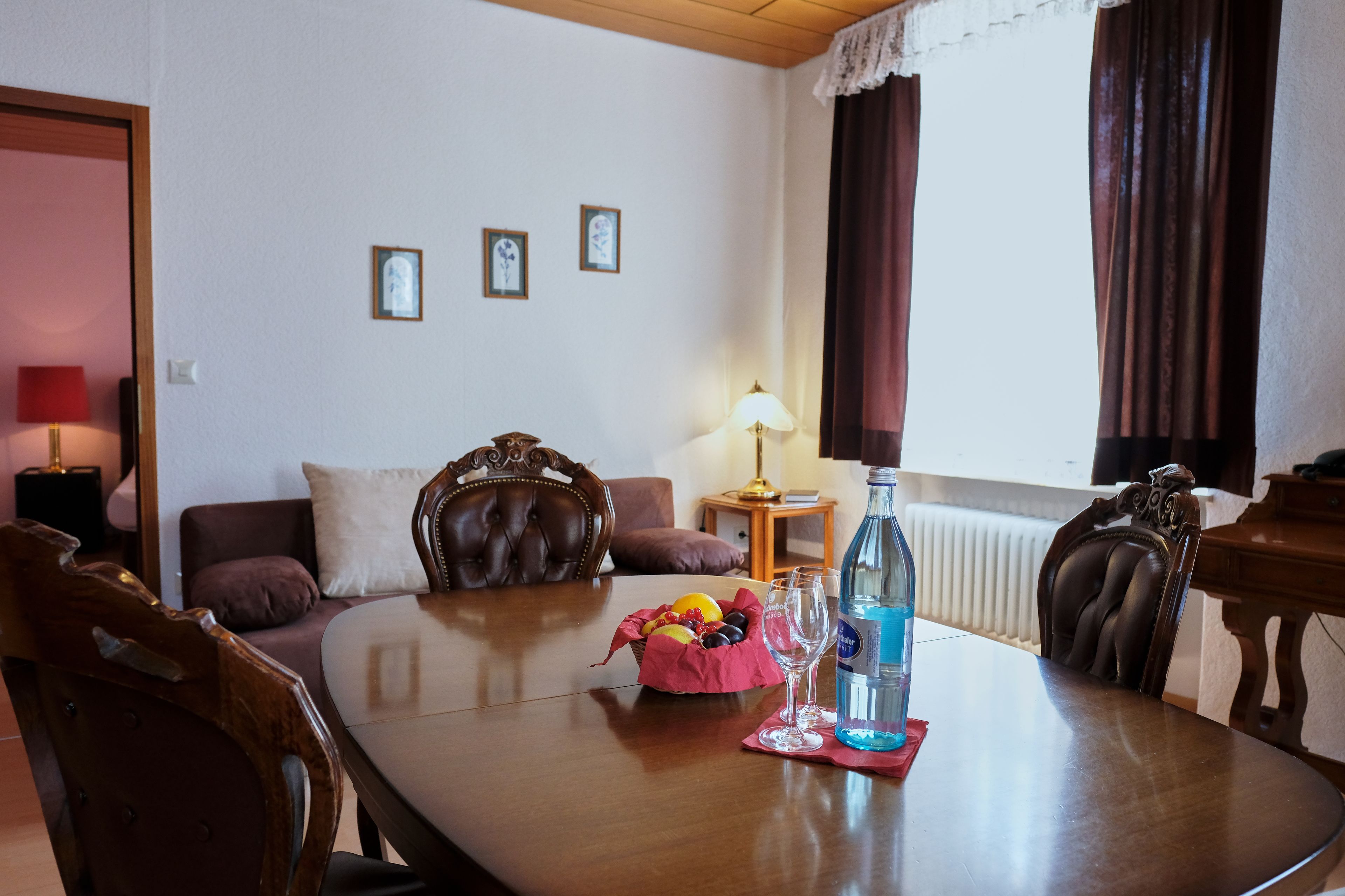 Un comedor con una mesa de madera, sillas, una cesta de frutas y una botella de agua.