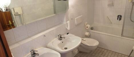 A bathroom with two sinks, a toilet, a shower, and a mirror with lights.