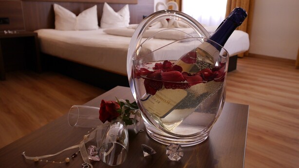 Hotelkamer met een bed, nachtkastje met champagne, rozenblaadjes en een decoratief glas.