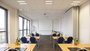 Un salón de conferencias con mesas, sillas y una pantalla para proyector.