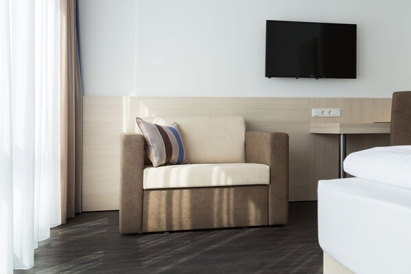 Una habitación de hotel moderna con sofá, televisor de pantalla plana en la pared y mesita de noche.