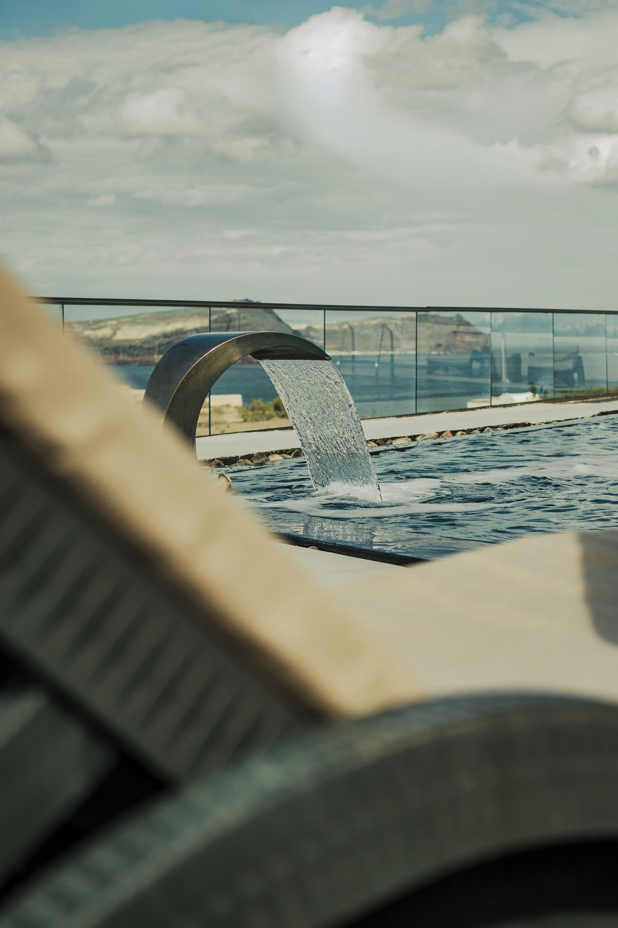 A water feature with a curved structure, a pool, and a distant view of a bridge and mountains.