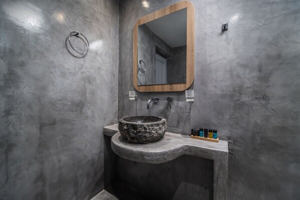 A bathroom with a stone sink, a wooden-framed mirror, and a towel ring. - Serenità Luxury Suites (Santorini)