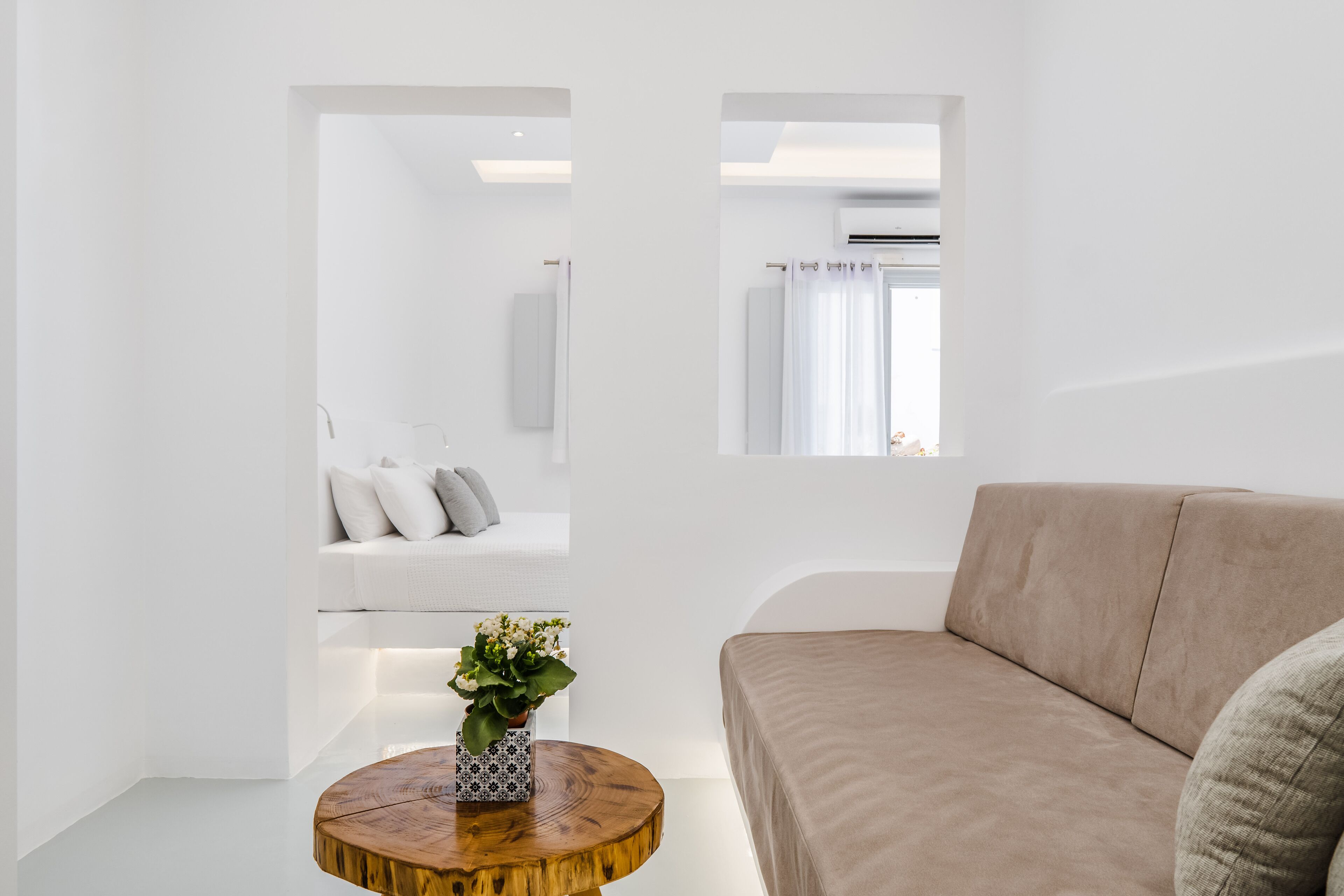 Una sala de estar moderna con un sofá color crema, una mesa de centro redonda de madera con un florero y una pared blanca con una lámpara empotrada.